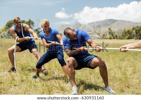 People playing tug of war during obstacle training course in boot camp