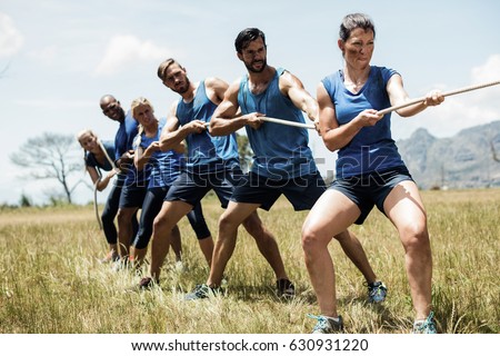 People playing tug of war during obstacle training course in boot camp