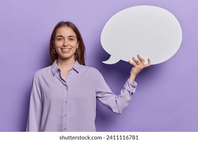 People positive emotions concept. Indoor photo of young pretty happy smiling European woman standing in centre isolated on purple background holding white speech bubble with space for promotion - Powered by Shutterstock