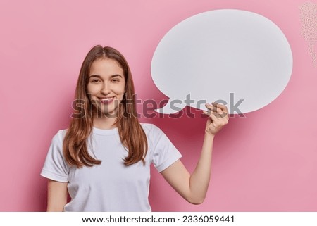 People positive emotions concept. Indoor photo of young beautiful smiling happy European female standing on left isolated on pink background holding speechbubble with blank space for promotion