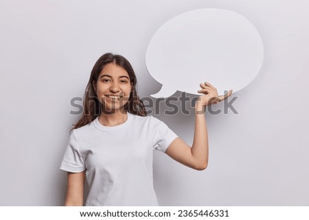 People positive emotions concept. Indoor waist up of pretty glad smiling Iranian female standing in centre isolated on white background in t shirt holding speech bubble with space for advertisement