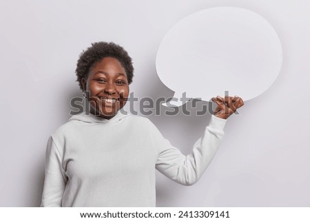 People positive emotions concept. Studio shot of young happy smiling broadly African american lady standing isolated on white background holding speech bubble with space for your advertisement