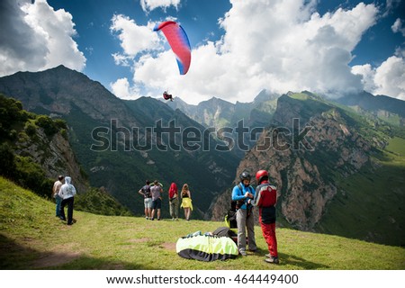 people are preparing for flight on a paraglider on a background of mountains, clouds and flying paraglider