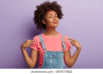 People, pride, arrogance concept. Self assured proud woman has Afro hairstyle satisfied with own high achievements, feels confident, keeps head raised, being like hero, isolated on purple wall