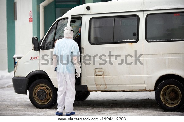 People in protective suits\
helping a sick person outdoors, coronavirus concept. Ambulance\
car.