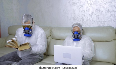 people in protective suits and respirators at home reading a book and using a laptop. - Powered by Shutterstock