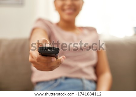 people, race, ethnicity and portrait concept - happy smiling african american young woman with remote control watching tv at home