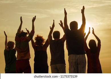 People raising hands up at the sky. Silhouette of family standing with hands up at the sunset.