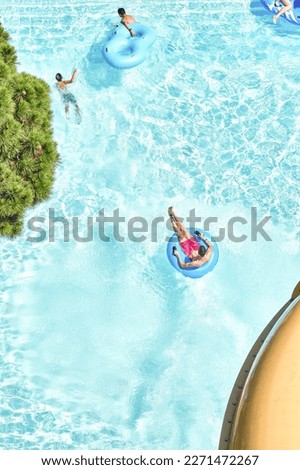 People relax on inflatable rubber rings in swimming pool with clear blue water. Fun activities in water park at summer resort upper view