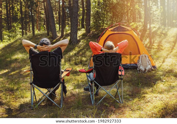 people relaxing in camping chairs at forest\
campsite and enjoying the\
nature