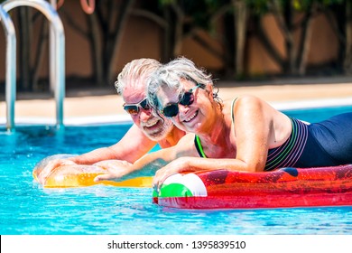 People retired old senior man and woman couple enjoying summer swimming pool leisure activity lay down on coloured trendy fashion lilos inflatable mattress on blue water at home or hotel activity - Powered by Shutterstock