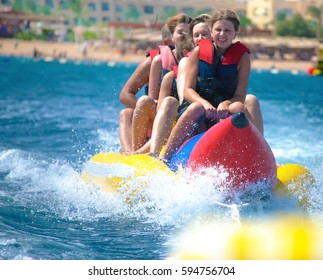 People Ride On Banana Boat On Sunny Summer Day. Beach Water Sport