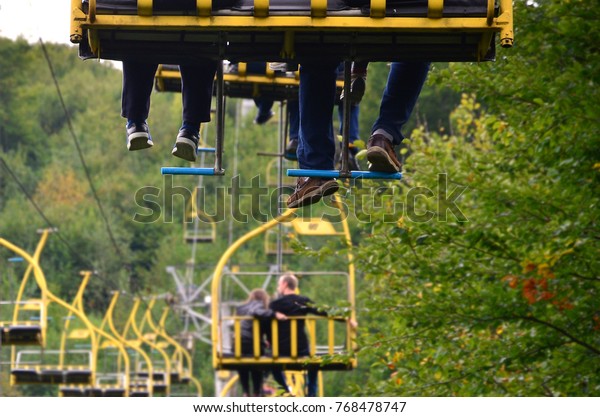 People ride on a cable car. The legs of passengers\
hang over the mountain\
forest
