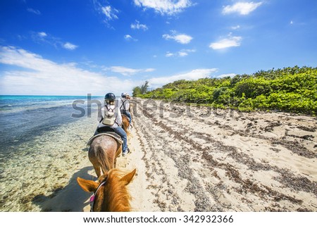 People riding on horse back at the Caribbean beach. Grand Cayman.