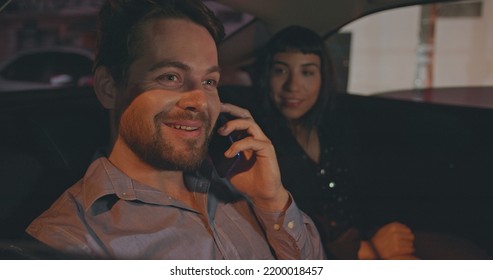 People Riding Taxi Cab In Car Backseat At Night. Young Man And Woman Passengers In The Evening After Work Talking On Phone