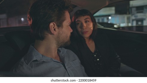 People Riding Taxi Cab Looking At Car Window At Night. Man Pointing Out Vehicle Glass With Girlfriend