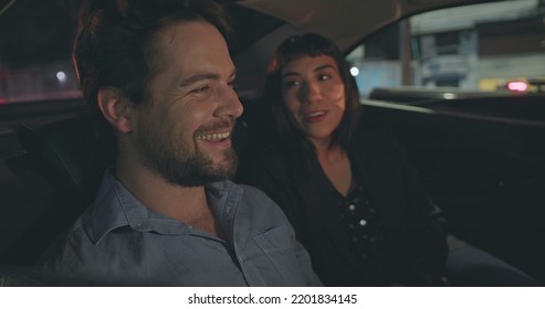 People Riding Taxi Cab Looking At Car Window At Night. Man Pointing Out Vehicle Glass With Girlfriend