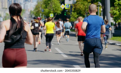 People Running Marathon, Focus On Man With Medical Mask Peeking Out Of His Pocket. Back View Crowd Of Contestants Competing In Sports Event During Pandemic