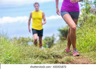 People Running Walking In Nature On Trail Path. Group Of Runners Hikers Hiking In Summer Outdoors. Woman Legs And Man In The Background. Fitness Activity For A Fit Couple Living A Healthy Lifestyle.