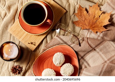 People, Season And Leisure Concept - Cup Of Coffee, Autumn Leaves, Meringues And Candle On Warm Blankets At Home