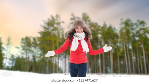 people, season and leisure concept - happy woman in fur hat outdoors over winter forest background
