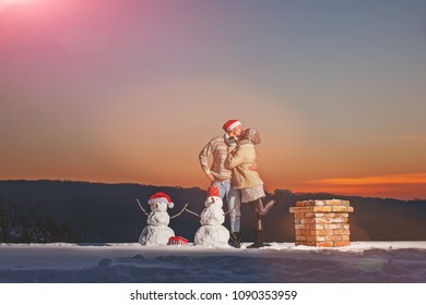 People, Season, Love And Leisure Concept - Happy Couple Hugging And Laughing Outdoors In Winter. Couple In Love. Christmas. Snowman. Kissing. Kiss. Love Story. Winter Day. Christmas Time. Santa Hats.
