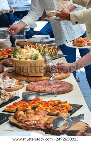People are serving themselves from a table full of italian cured meat, cheese and other delicious food during a catered event