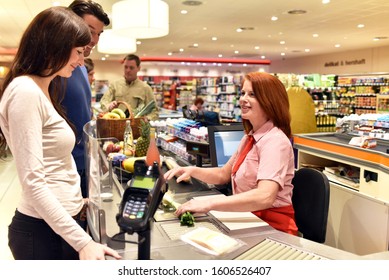 People Shopping At The Supermarket - Paying At The Checkout With A Friendly Cashier