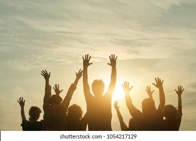 People silhouette at sunset. Happy fans of a rock group outdoor. Human body over natural colorful sky background.