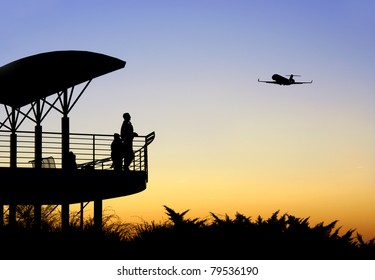 People In Silhouette Watching An Airplane Take Off