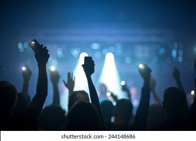 People Silhouettes With Raised Hands Holding Phones With Flashlights Enjoying A Concert At Nightclub