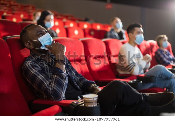People sit in the cinema hall and watch a movie\
wearing medical masks and keep their distance. Covid-19 and the\
film industry