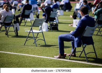 People Sit On Chairs Apart One From Another To Maintain The Social Distance During The Covid-19 Outbreak At An Outdoor Event On The Turf Of A Stadium.