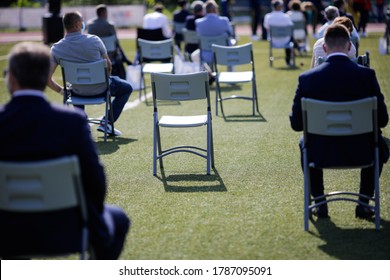 People Sit On Chairs Apart One From Another To Maintain The Social Distance During The Covid-19 Outbreak At An Outdoor Event On The Turf Of A Stadium.