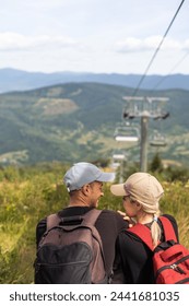 People sit on the ski elevator. View from the back. Summer, green forest. summer family vacation in the mountains.