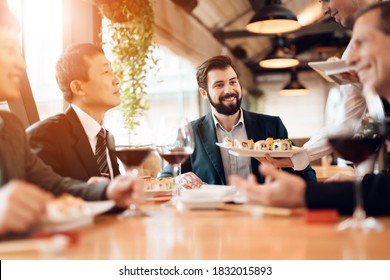 People sit at a table eating sushi and drinking wine. The waiter brings sushi to business people who stipulate business ideas in a restaurant.
