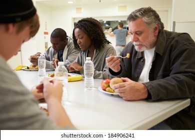 People Sitting At Table Eating Food In Homeless Shelter