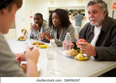 People Sitting At Table Eating Food In Homeless Shelter