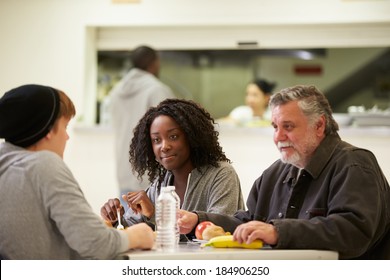 People Sitting At Table Eating Food In Homeless Shelter