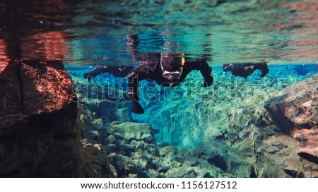 People Snorkeling swimming diving in the blue cold glacier water in famous fissure Silfra between two tectonic plates in the national park Thingvellir in Iceland. Blue transparent water, deep colors.