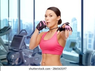 People, Sport, Fitness And Healthy Lifestyle Concept - Asian Woman Coach Blowing Whistle Over Gym Machines Background