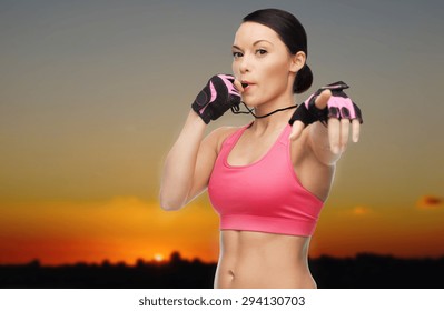 People, Sport, Fitness And Healthy Lifestyle Concept - Happy Asian Woman Coach Blowing Whistle Outdoors Over Sunset Skyline Background