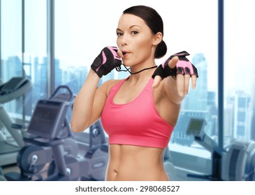 People, Sport, Fitness And Healthy Lifestyle Concept - Asian Woman Coach Blowing Whistle Over Gym Machines Background