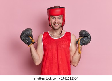 People sport motivation concept. Positive man has training in gym wears protective headgear boxing gloves t shirt has cheerful expression after winning sport game isolated over pink background - Powered by Shutterstock