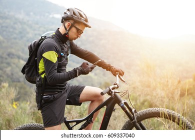 People, sports, active lifestyle and modern technology. Outdoor picture of cyclist on booster bike using navigator on smart phone, exploring map and searching GPS coordinates while biking in mountains