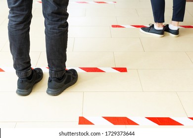 People Stand In Line Keeping Social Distance, Standing Behind A Warning Line During Covid 19 Coronavirus Quarantine. Safe Shopping, Social Distancing Concept. Legs In Line Close Up