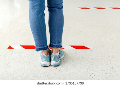 People Stand In Line Keeping Social Distance, Woman Standing Behind A Warning Line During Covid 19 Coronavirus Quarantine. Safe Shopping, Social Distancing Concept. Legs In Line Close Up