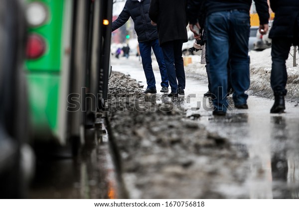 people are standing at a bus stop, getting on a bus
stepping over uncleared snow and mud, special services do not clean
the city