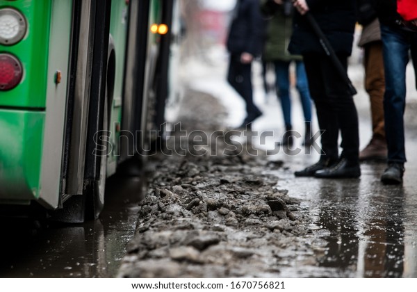 people are standing at a bus stop, getting on a bus\
stepping over uncleared snow and mud, special services do not clean\
the city