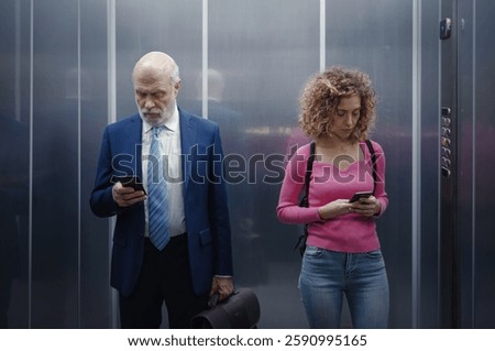 People standing inside the elevator, they are using their smartphones and ignoring each other
